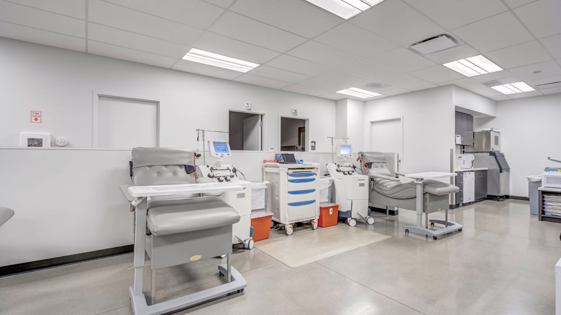 A clean, modern medical facility room—crafted with the precision of commercial construction standards—features several reclining chairs, medical equipment, monitors, and white walls. Designed for patient treatments such as blood donation or dialysis, this thoughtfully planned space reflects the meticulous attention to detail found in today’s commercial building projects.